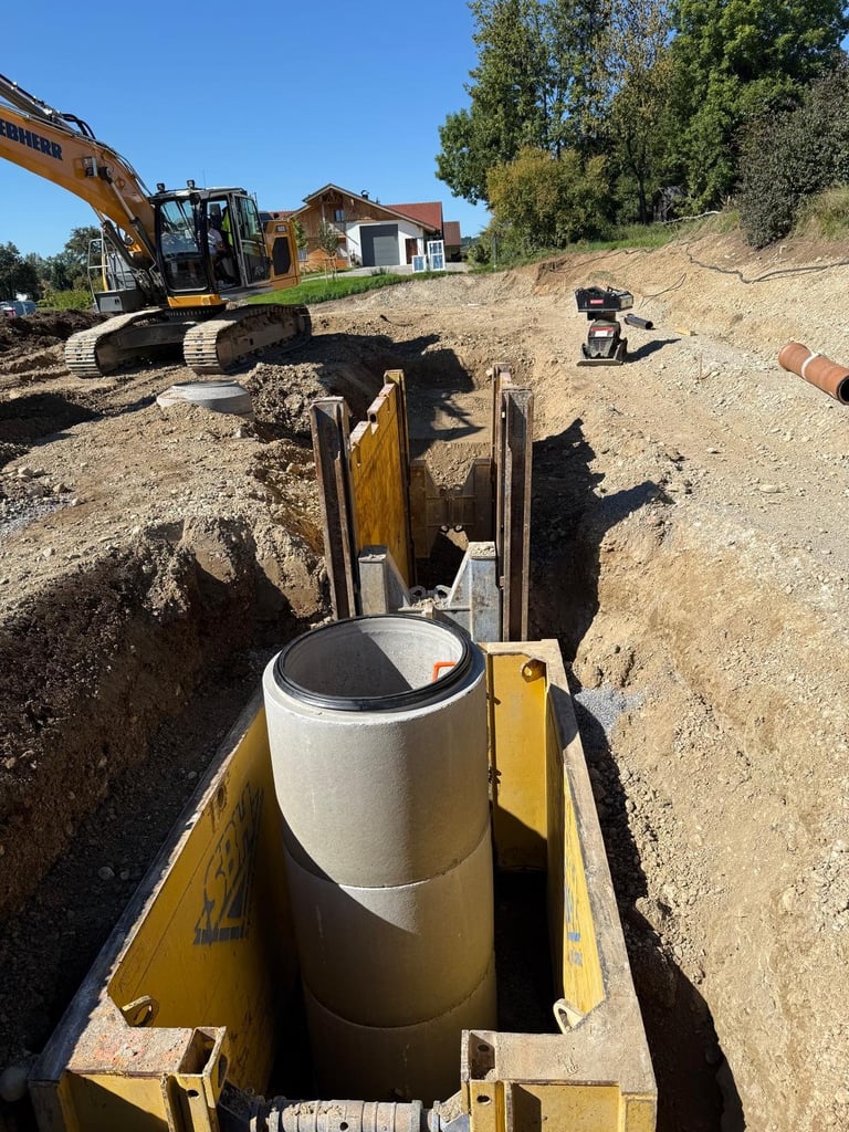 Baustelle mit Bagger und Arbeitern beim Einbau eines großen Betonrohrs in einem unterirdischen Graben