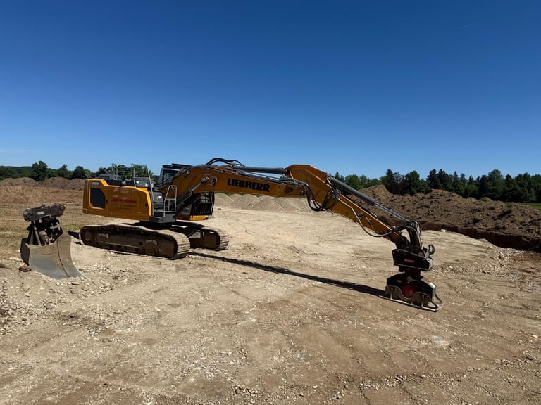 Zwei gelbe Bagger auf einer sandigen Baustelle mit Erdhaufen und Bäumen im Hintergrund unter klarem blauem Himmel