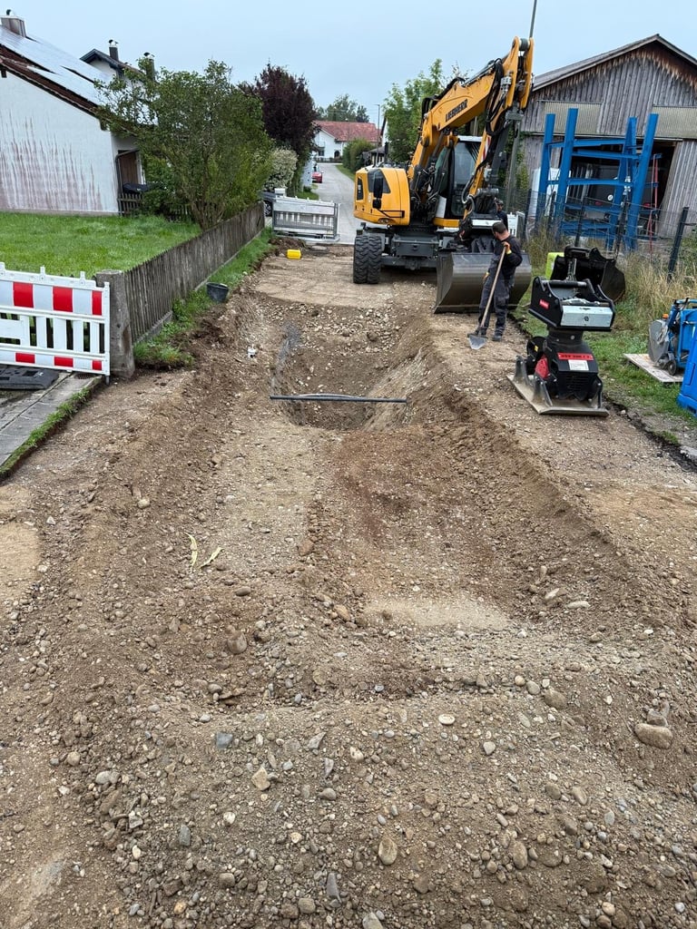Baustelle mit gelbem Bagger und schweren Maschinen auf Erdweg, rot-weißer Absperrzaun links sichtbar