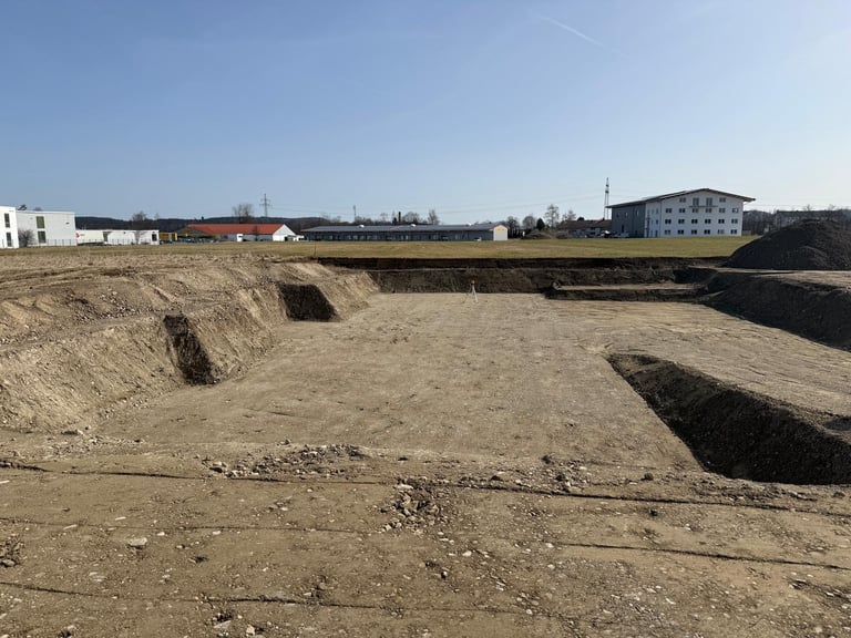 Baustelle mit ausgehobenen Erdhaufen, Industriegebäuden und blauem Himmel im Hintergrund