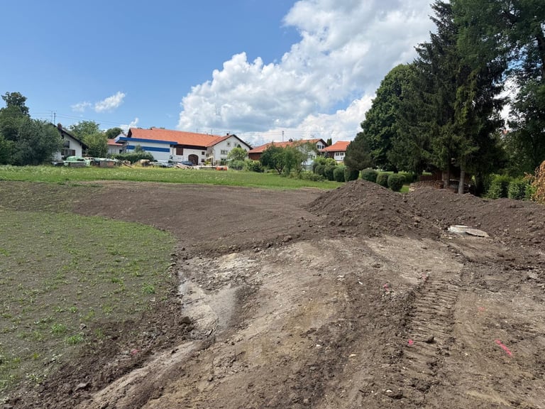 Frisch bearbeitetes Ackerland mit Bauernhäusern und Bäumen im Hintergrund