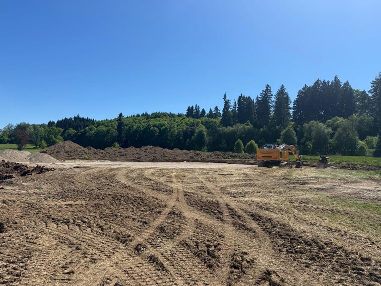 Traktor bei der Arbeit auf gepflügtem Ackerfeld mit dichtem Nadelwald im Hintergrund unter klarem blauem Himmel