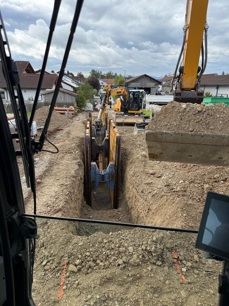 Baustelle mit gelben Baggern und Maschinen beim Ausheben von Gräben in sandigem Boden, Wohngebiet im Hintergrund