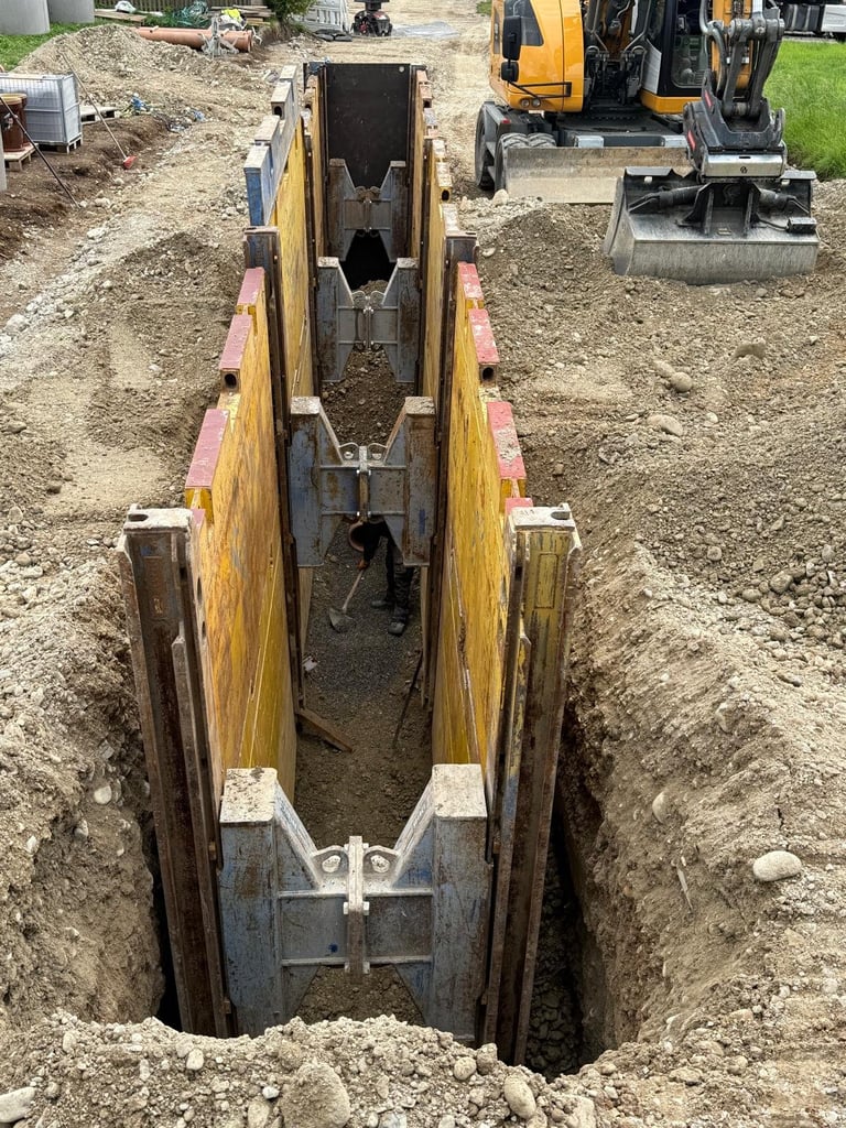 Tiefer Graben mit gelben und roten Holzverbauplatten und Metallstützen auf einer Baustelle
